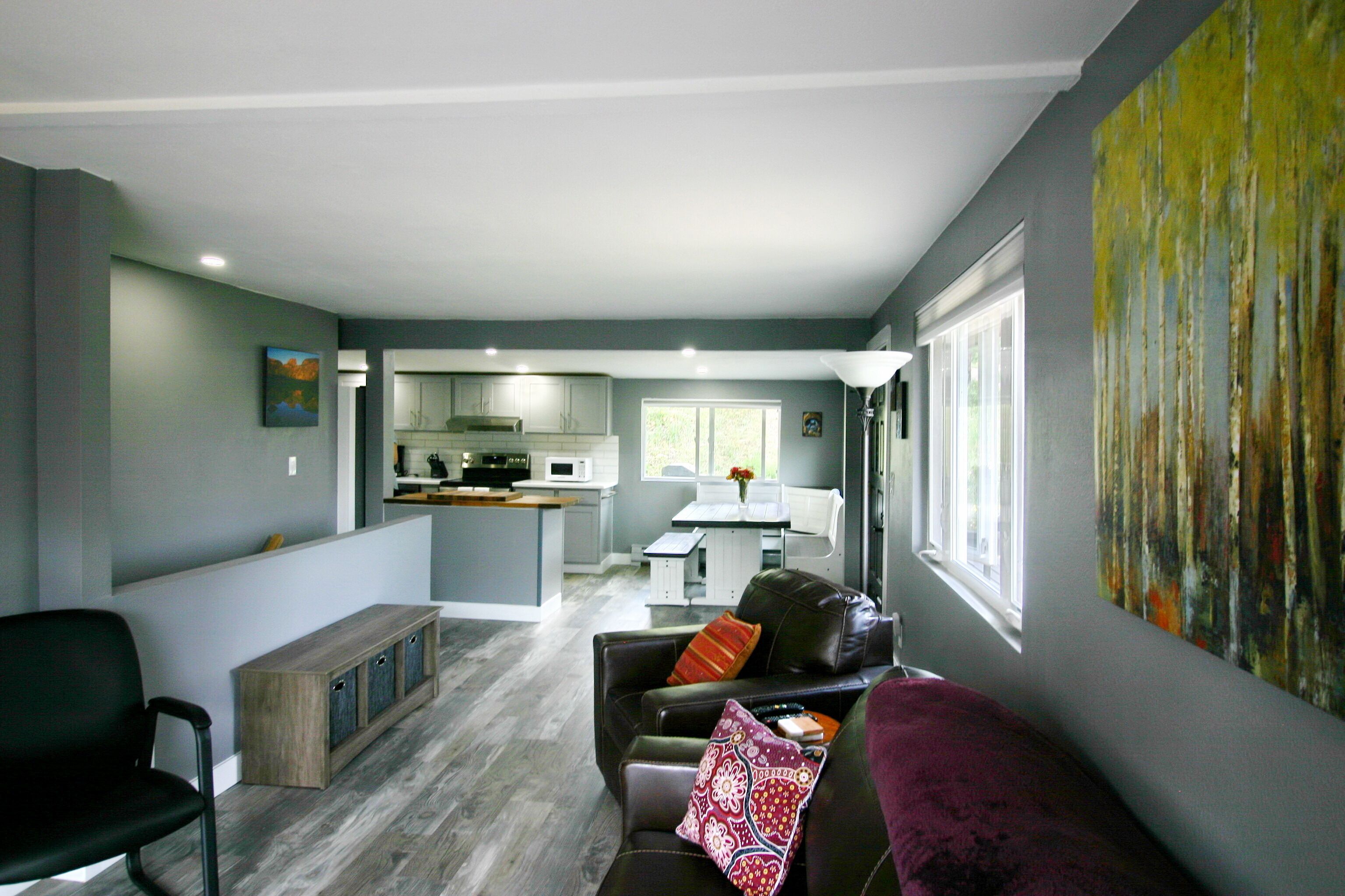 Un salon moderne avec un canapé en cuir foncé, un banc en bois et un tableau abstrait aux couleurs vives accroché au mur.