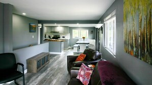 Un salon moderne avec un canapé en cuir foncé, un banc en bois et un tableau abstrait aux couleurs vives accroché au mur.