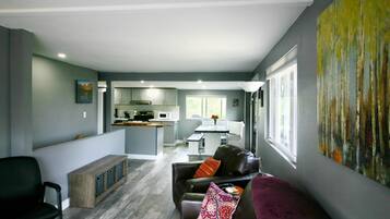 Un salon moderne avec un canapé en cuir foncé, un banc en bois et un tableau abstrait aux couleurs vives accroché au mur.