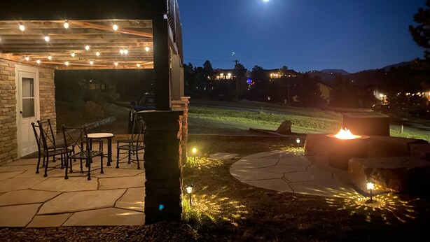 Un espace extérieur aménagé en terrasse, avec un sol en pierre, un foyer et des guirlandes lumineuses.