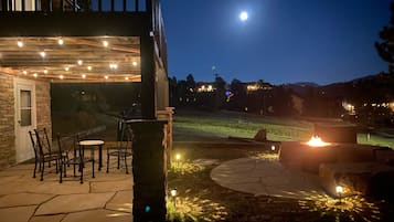 Un espace extérieur aménagé en terrasse, avec un sol en pierre, un foyer et des guirlandes lumineuses.