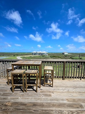 A wooden deck with outdoor furniture, a view of a house and landscape in the background.