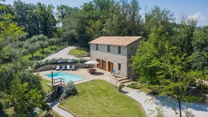 Une maison en pierre avec une piscine, entourée d’une pelouse bien entretenue et d’arbres.