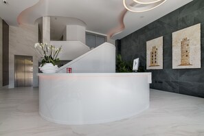 A modern reception area with a curved white counter, a staircase, and artwork on the walls. - TH Apartments by Como en Casa (A Coruña)
