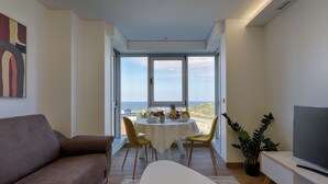A modern living room with a sofa, a dining table with chairs, a TV, and a view of the sea through large windows. - TH Apartments by Como en Casa (A Coruña)