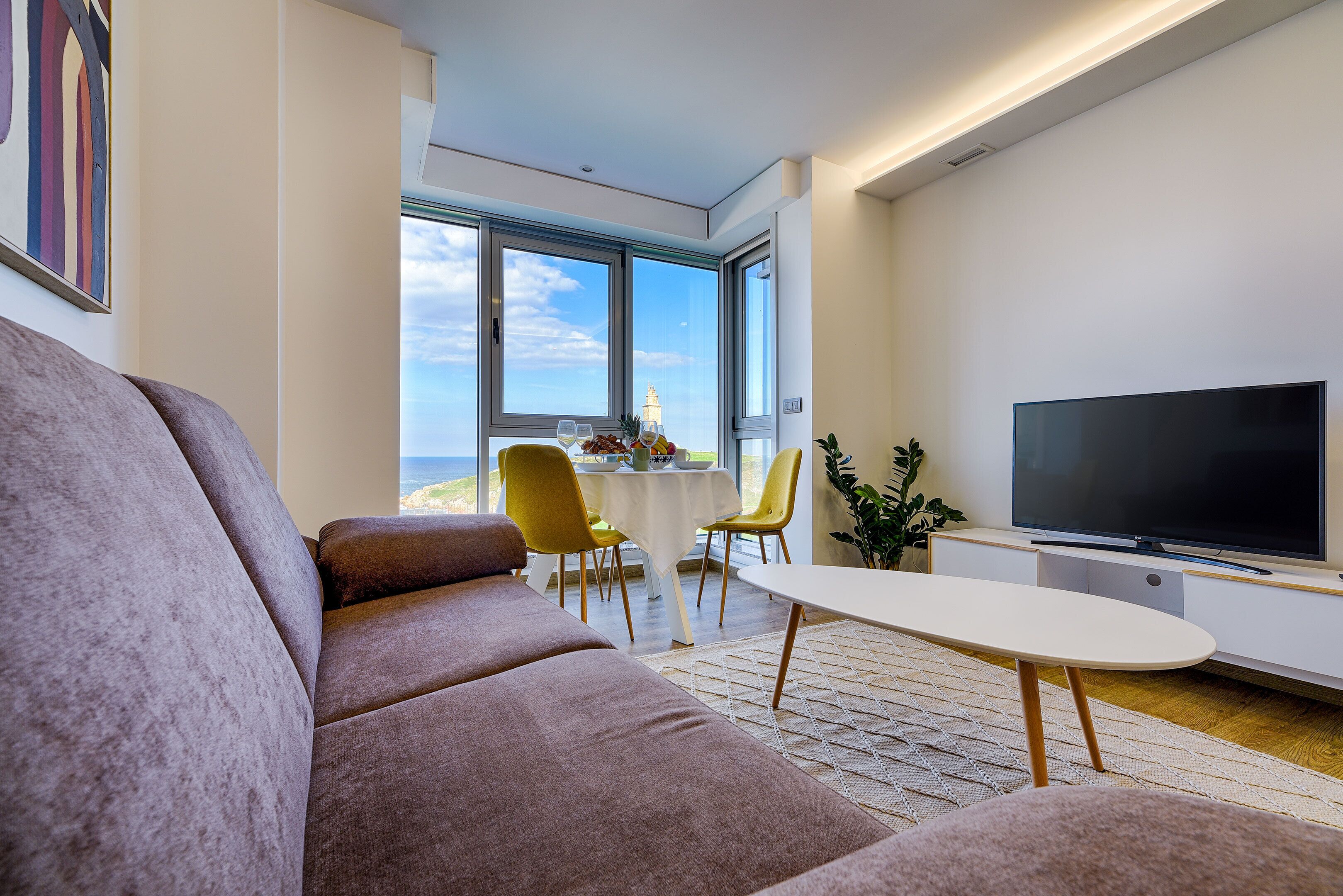 A modern living room with a sofa, a dining table with chairs, and a flat-screen TV.