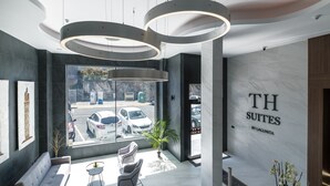 A modern hotel reception area with a large window, a seating area with two chairs, and a wall with the text "TH SUITES BY LAGUNITA". - TH Apartments by Como en Casa (A Coruña)