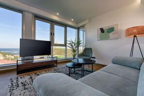 A modern living room with a large TV, comfortable seating, a small table, and a view of the ocean. - TH Apartments by Como en Casa (A Coruña)