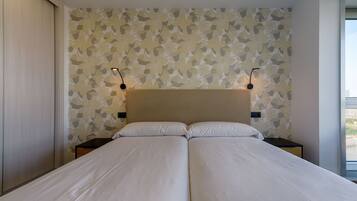 A double bed with a beige headboard, two bedside tables with lamps, and a patterned wallpaper.