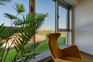 A room with a large window, a yellow chair, and a view of a building and green landscape. - TH Apartments by Como en Casa (A Coruña)