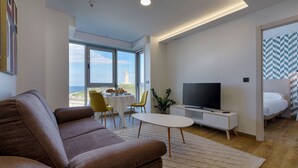 A modern living room with a sofa, a TV, a dining table with chairs, and a view of the sea. - TH Apartments by Como en Casa (A Coruña)