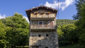 A stone tower with a wooden balcony, surrounded by lush greenery and a clear sky. - Cosy flat for nature lovers and peace seekers in the mountain village of Livo (Livo)
