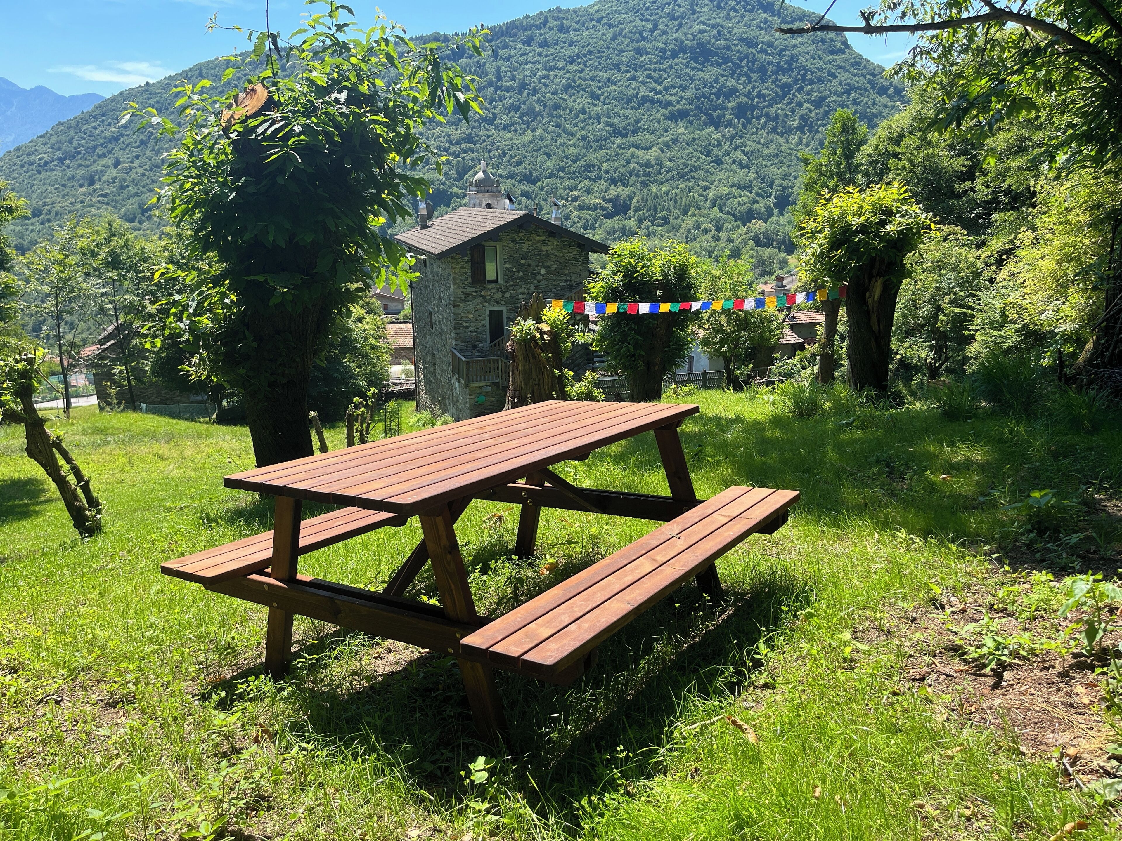 A picnic table in a grassy area with a stone building and a mountain in the background.
