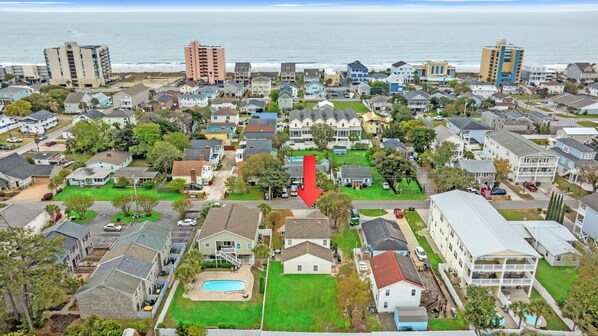 A residential area with houses, a large red arrow pointing to a specific house, and a beach in the background.