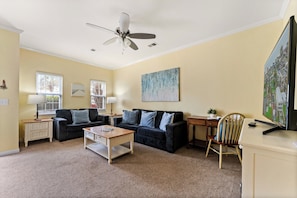 A living room with a ceiling fan, two couches, a coffee table, a TV, and a desk.