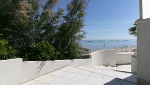 Un escalier menant à un balcon d’où l’on a une vue sur une plage, avec un ciel dégagé.