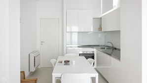 Une cuisine moderne avec des meubles blancs, une table à manger, des chaises et un four encastré.