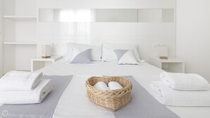 Une chambre d’hôtel avec un grand lit, deux tables de chevet, un panier en osier contenant des serviettes et une vue sur le ciel par la fenêtre.