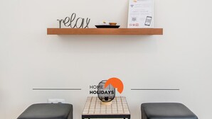 A minimalist room with a wooden shelf displaying a 'relax' sign, a small table with a decorative item, and two black ottomans. - #055 São José V by Home Holidays (Albufeira)