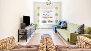 A modern living room with a sofa, a TV on a stand, and a large window with a view of buildings. - #055 São José V by Home Holidays (Albufeira)