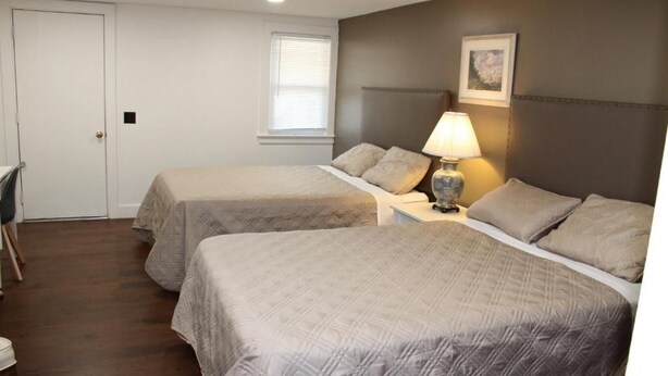 Une chambre d’hôtel avec deux lits, un bureau, une chaise, une lampe et une fenêtre avec des stores.