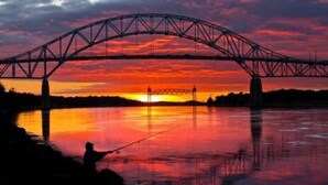La silhouette d’une personne pêchant sous un pont au coucher du soleil.
