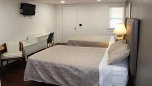 Une chambre d’hôtel avec deux lits, un bureau, une chaise, un téléviseur fixé au mur et une fenêtre avec des stores.