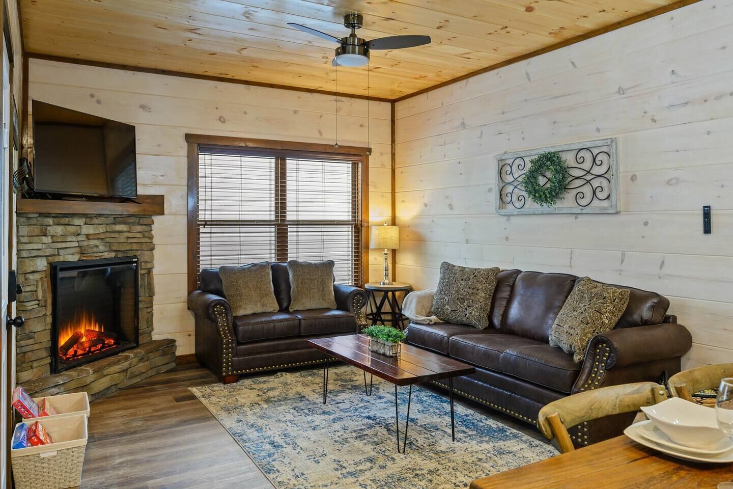 A cozy living room with a stone fireplace, leather sofas, a coffee table, and a dining area with a table and chairs.