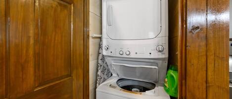 A compact washer and dryer unit in a wooden cabinet with a green detergent bottle beside it.