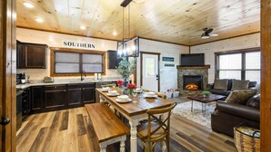 A cozy interior with a wooden ceiling, a kitchen with dark cabinets, a dining area with a wooden table and chairs, a fireplace, and a living room with a sofa and a TV. - Private Indoor Pool Cabin | Arcade, Hot Tub | 1.5mi to Parkway (Pigeon Forge)