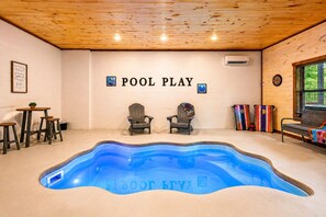 Une piscine à la forme originale, deux fauteuils Adirondack, un jeu de fléchettes et un mur sur lequel on peut lire les mots « POOL PLAY ».