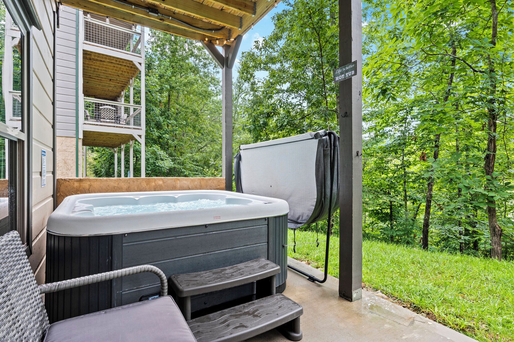 Ein Whirlpool mit Stufen und einer überdachten Sitzgelegenheit, umgeben von üppiger Vegetation und einer Holzterrasse.