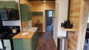 Een compacte keuken met groene kastjes, een houten aanrecht, een afvalbak van roestvrij staal en een koffiezetapparaat op een plankje.