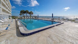 Ein Pool mit Liegestühlen und Palmen, ein klarer Himmel und Blick auf den Ozean.