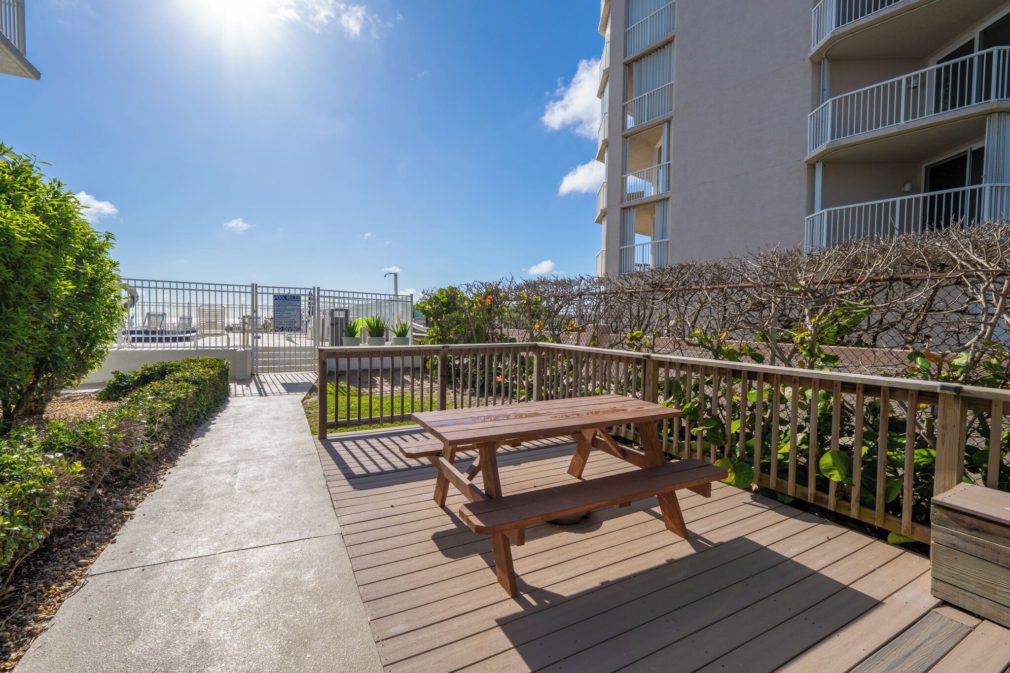 A wooden deck with a picnic table, a metal fence, and a building with balconies.