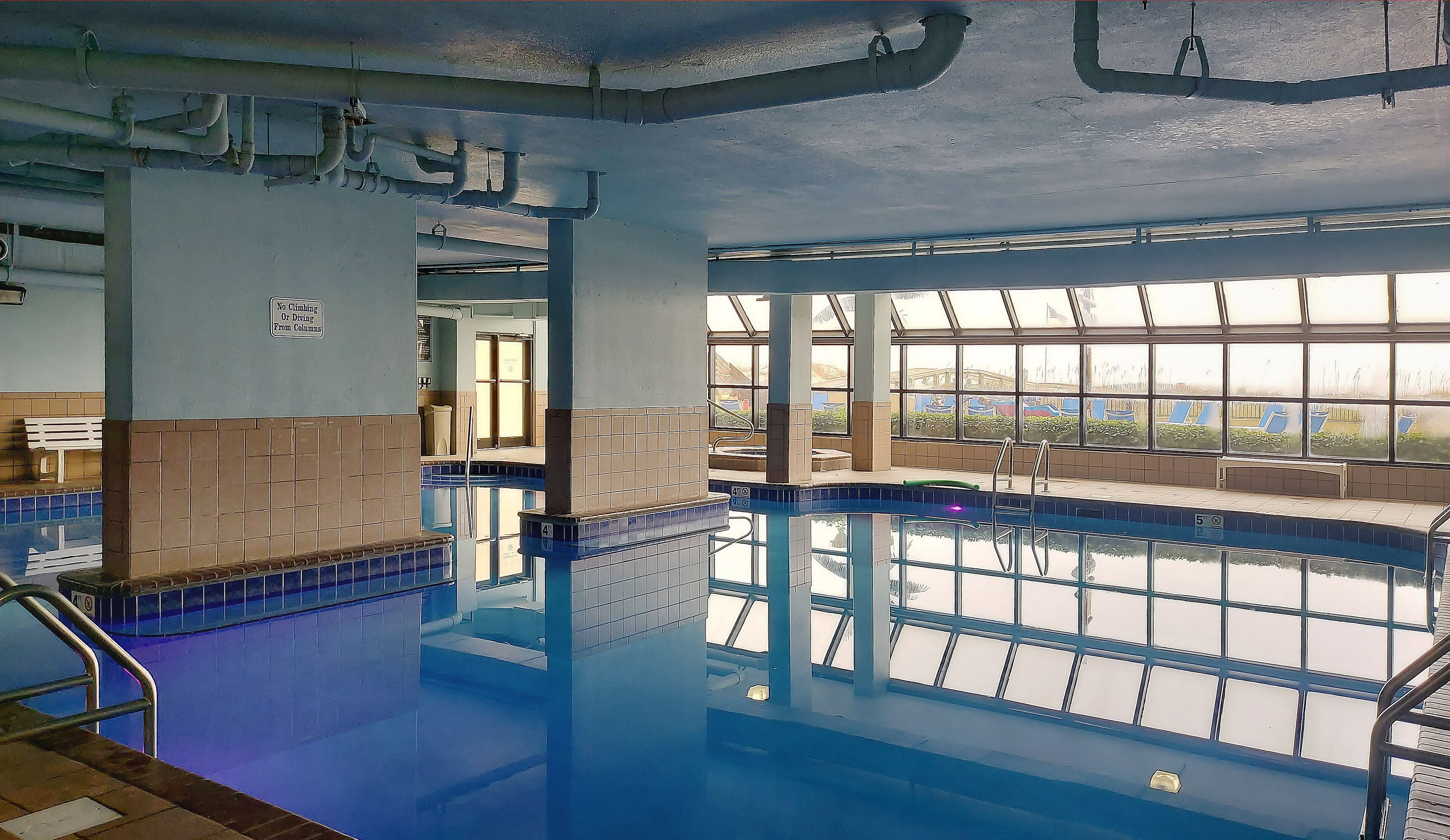 Une piscine intérieure à l’eau d’un bleu limpide, avec des murs carrelés et de grandes fenêtres laissant entrer la lumière naturelle.