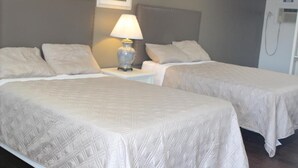 Una camera d'albergo con due letti, un comodino con lampada e un angolo doccia.