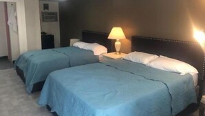 Camera d'albergo con due letti singoli, un comodino con una lampada, un armadio e una porta che dà su un'altra stanza.