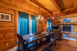 A wooden cabin interior with a dining table, benches, a sofa, a fireplace, and a mounted television. - Hillside Heaven - Hot tub, pool table, firepit (Boone)