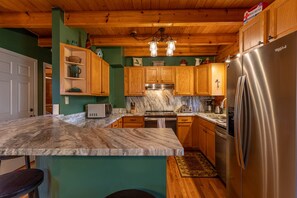 A kitchen with wooden cabinets, a stainless steel refrigerator, a marble countertop, and a wooden ceiling. - Hillside Heaven - Hot tub, pool table, firepit (Boone)