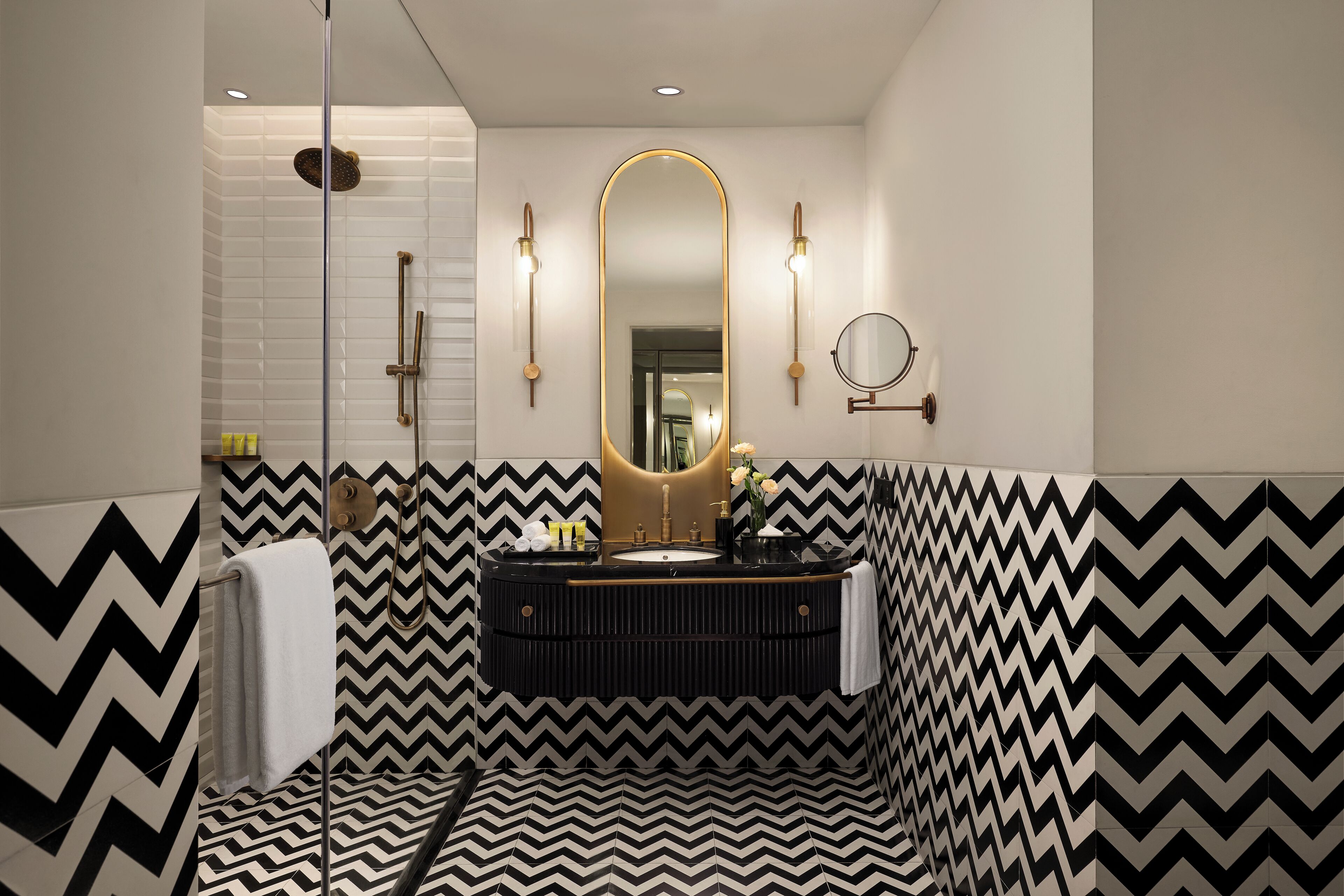 Un baño moderno con un patrón geométrico blanco y negro en forma de chevron, un espejo grande y una lámpara redonda empotrada en la pared.