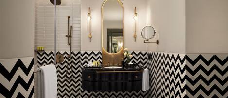 Un baño moderno con un patrón geométrico blanco y negro en forma de chevron, un espejo grande y una lámpara redonda empotrada en la pared.