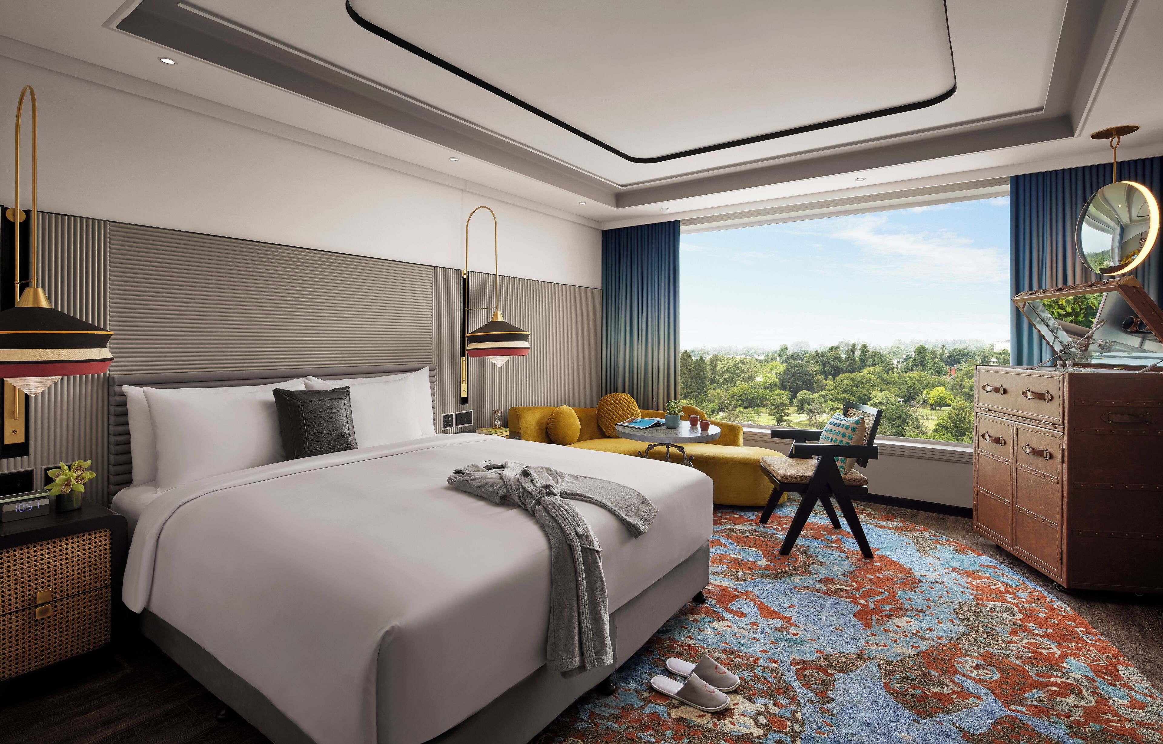 A modern hotel room with a large bed, a sofa, a desk, and a dresser.