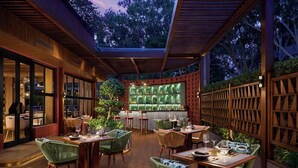 Een eetruimte met houten tafels en stoelen, een bar met groene planken en een grote boom in het midden.