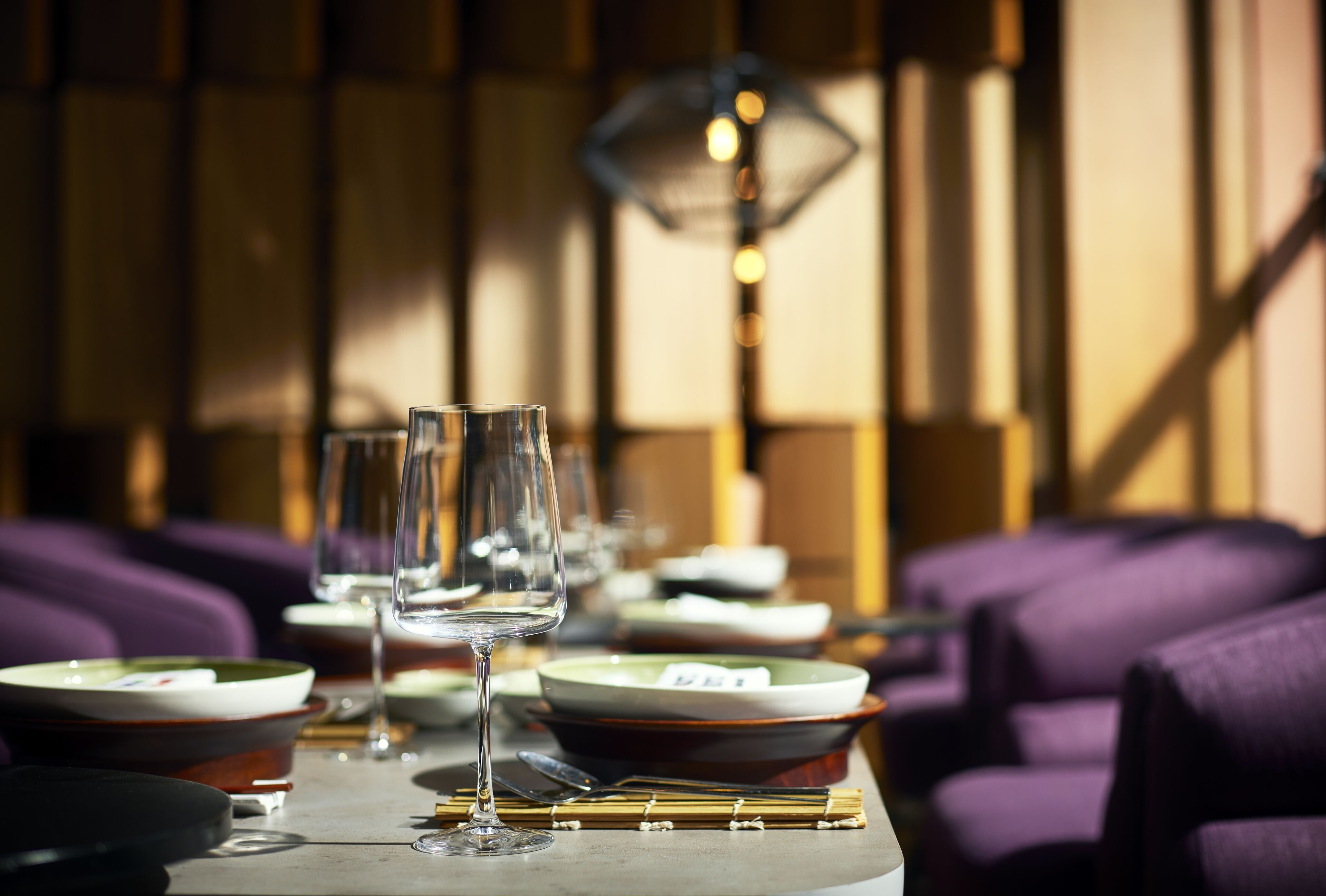 A dining table set with plates, bowls, and wine glasses, with purple upholstered chairs in the background.