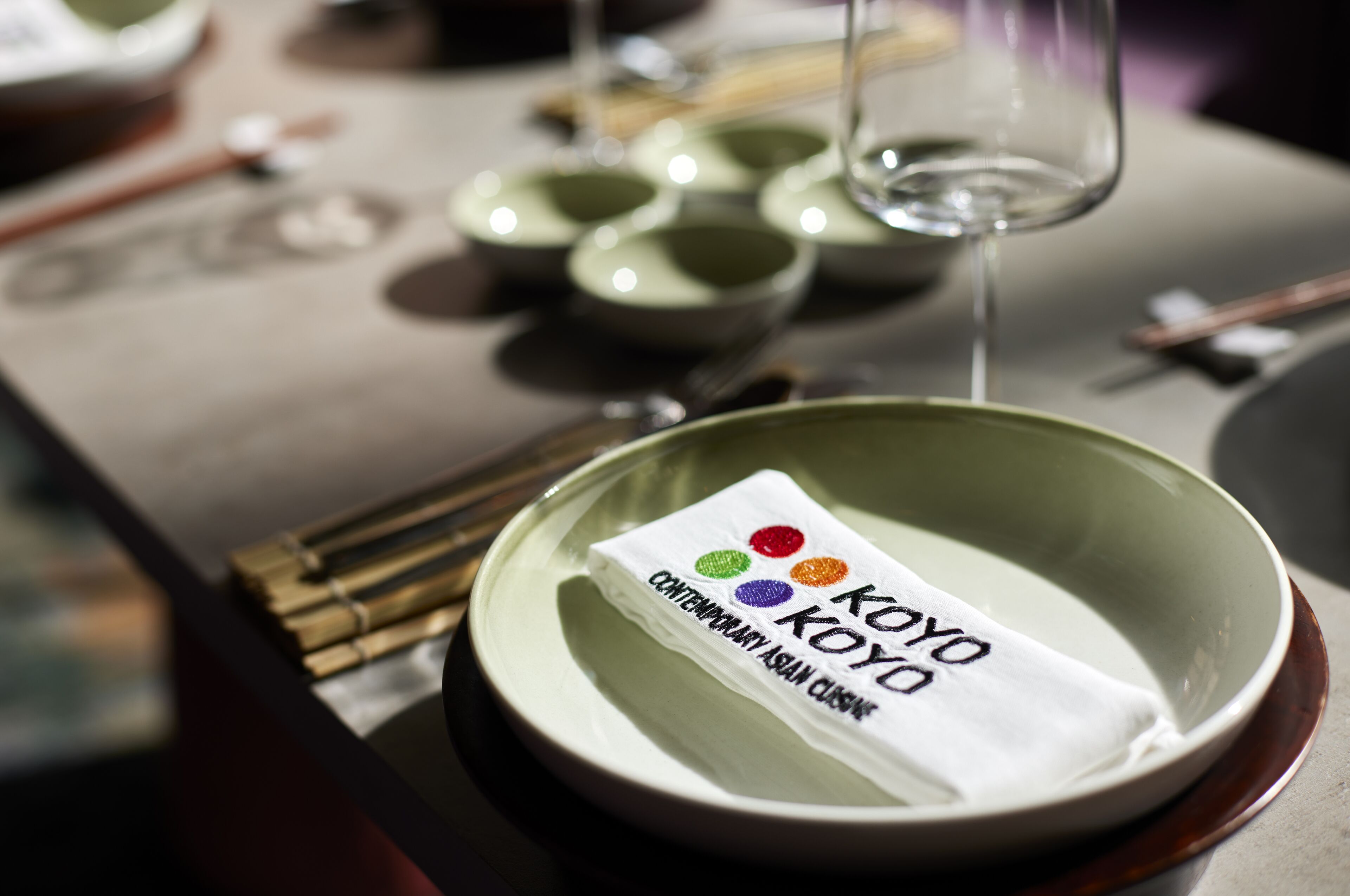 A table setting with a green bowl, chopsticks, and a napkin with the text "KOYO CONTEMPORARY ASIAN CUISINE".