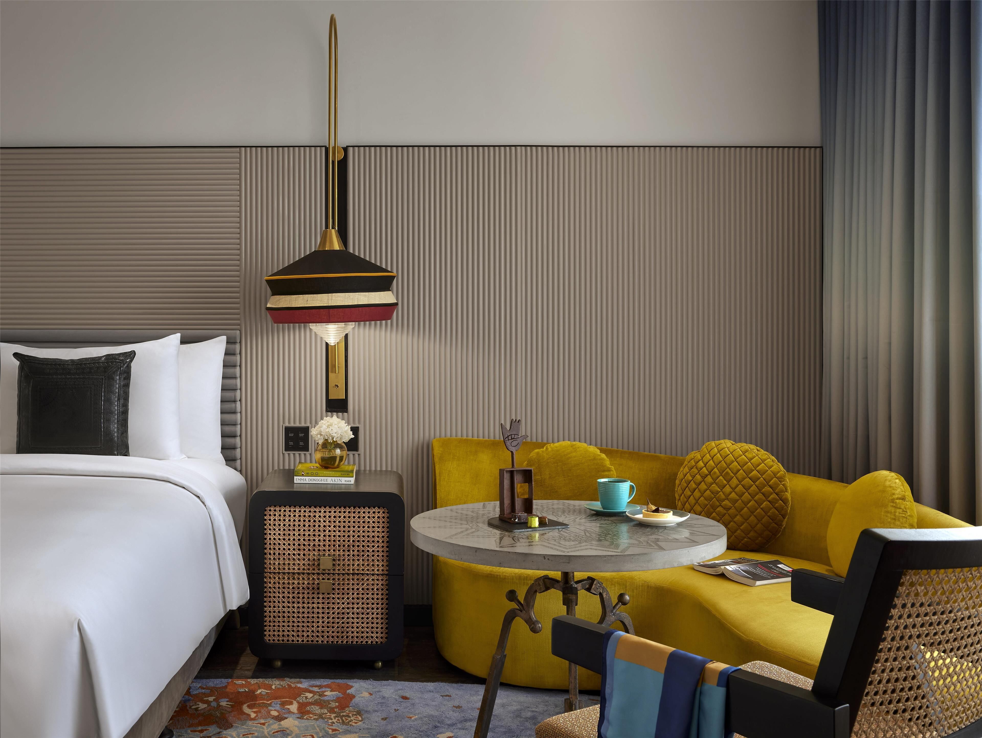 A hotel room with a bed, a round table, a yellow sofa, and a decorative lamp.