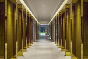 Un pasillo moderno con paredes reflectantes y piso pulido, que conduce a una puerta de vidrio.