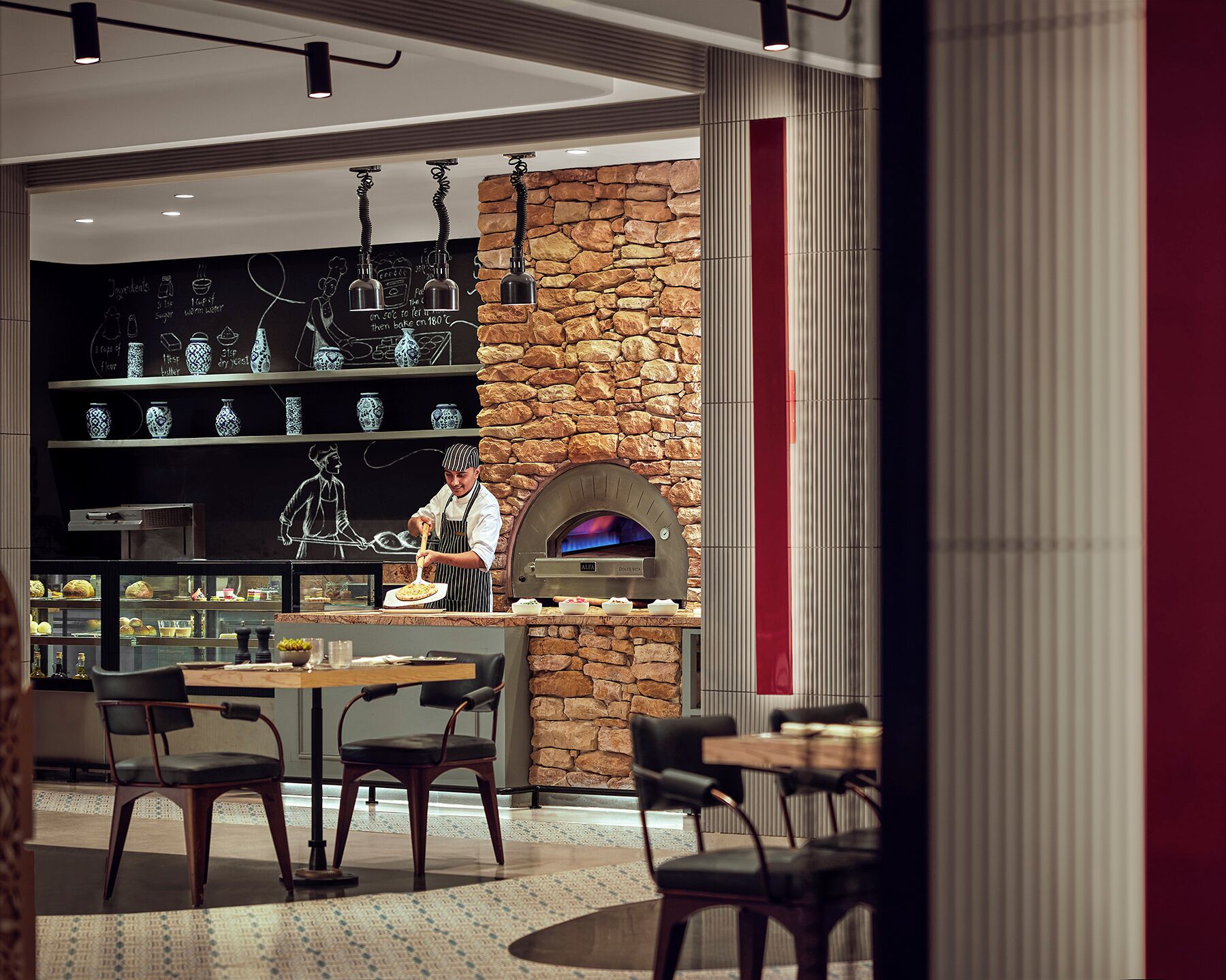 A modern restaurant with a stone wall and a pizza oven. There are tables and chairs for dining.