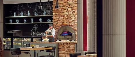 A modern restaurant with a stone wall and a pizza oven. There are tables and chairs for dining.